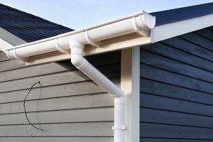 Gutter cleaning in Monroe, white gutter downspout and elbow on blue house